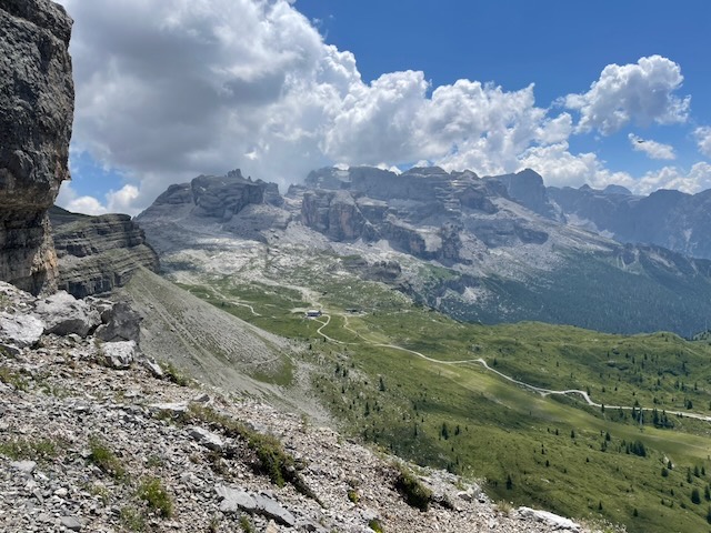 Brentské Dolomity z sedla nad Lago di Garda, s chatou a turistickými cestami vinoucími se zelenou kotlinou pod nimi